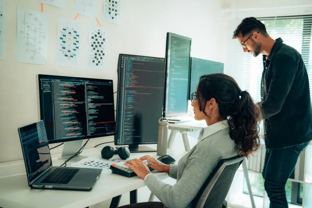 A close up of a dual monitor developer workstation showing terminal commands and script compilation